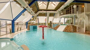 Une piscine intérieure dotée d’un élément décoratif central aquatique, de murs en pierre et d’un plafond en verre.