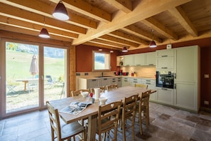 Uma cozinha espaçosa com vigas de madeira, uma área de jantar com mesa e cadeiras, e vista para uma área externa gramada.
