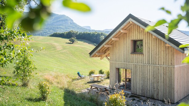 A wooden cabin with a patio, surrounded by a grassy field and mountains in the background. - Apartment 'Le Chalet De La Source' with Mountain View, Private Terrace and Wi-Fi (Montagnole)