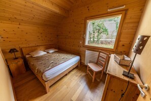 Une petite chambre d’une cabane, chaleureuse et accueillante, avec un lit simple, une chaise, un bureau et une fenêtre.