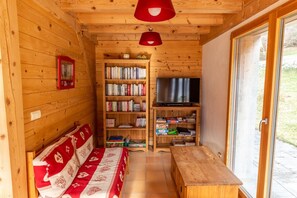 Interior acogedor de una cabaña con un banco de madera, una estantería, un televisor y un ventanal corredero.