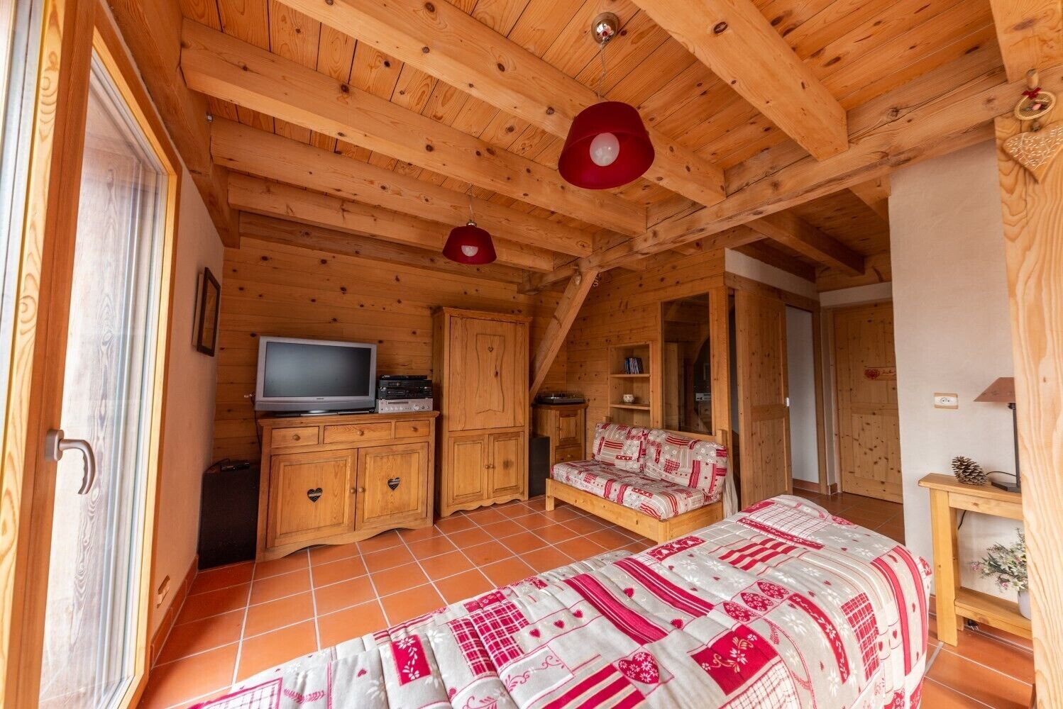 A wooden cabin interior with a bed, a television, and a wardrobe.