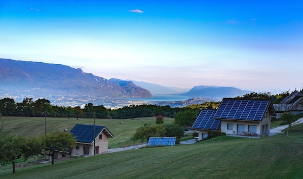 Une maison équipée de panneaux solaires, un champ verdoyant et des montagnes en arrière-plan.