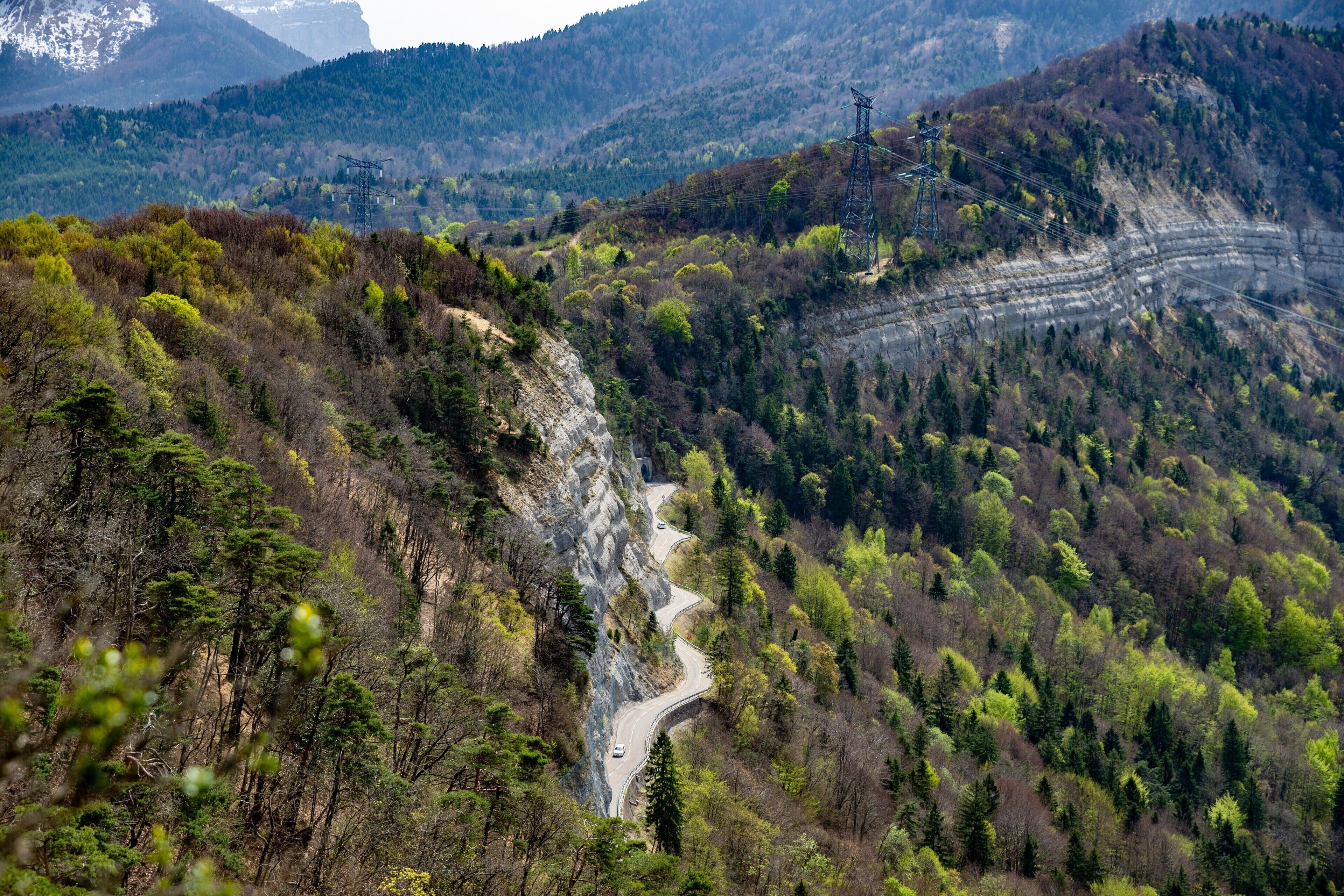 Une route de montagne sinueuse, bordée d’une forêt dense et traversant un terrain rocheux.