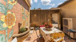 Une terrasse extérieure avec un mur recouvert de carreaux, une table avec des chaises, une plante en pot et un appareil de climatisation.