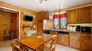 A wooden kitchen with a dining table, chairs, cabinets, a stove, and a television.