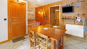 A wooden-paneled room with a dining table, chairs, a television, and a fireplace.