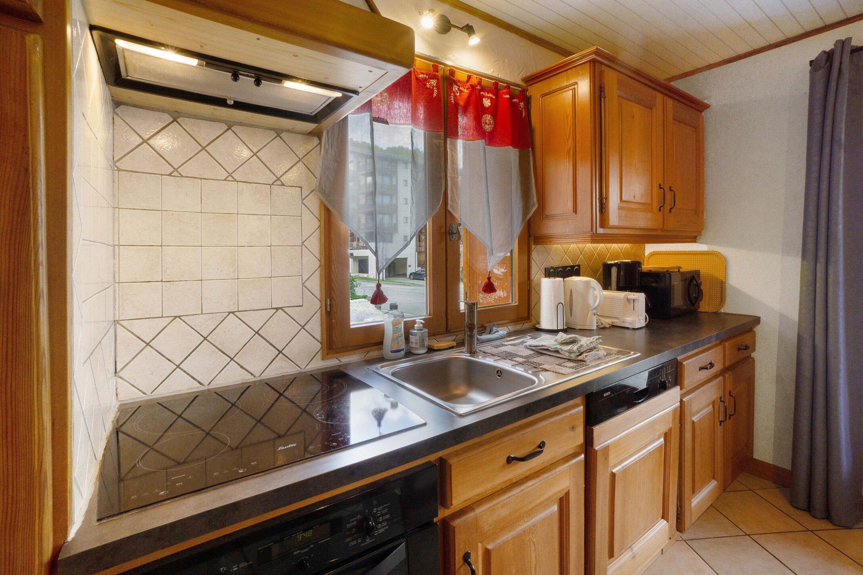 A kitchen with a dishwasher, stove, sink, wooden cabinets, and a window with curtains.