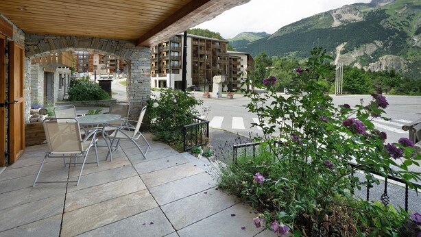 A covered outdoor area with a stone archway, a patio table with chairs, and a view of a mountain landscape.