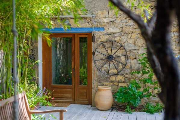 Une porte en bois avec des panneaux de verre, un mur en pierre, une grande roue et une terrasse en bois.