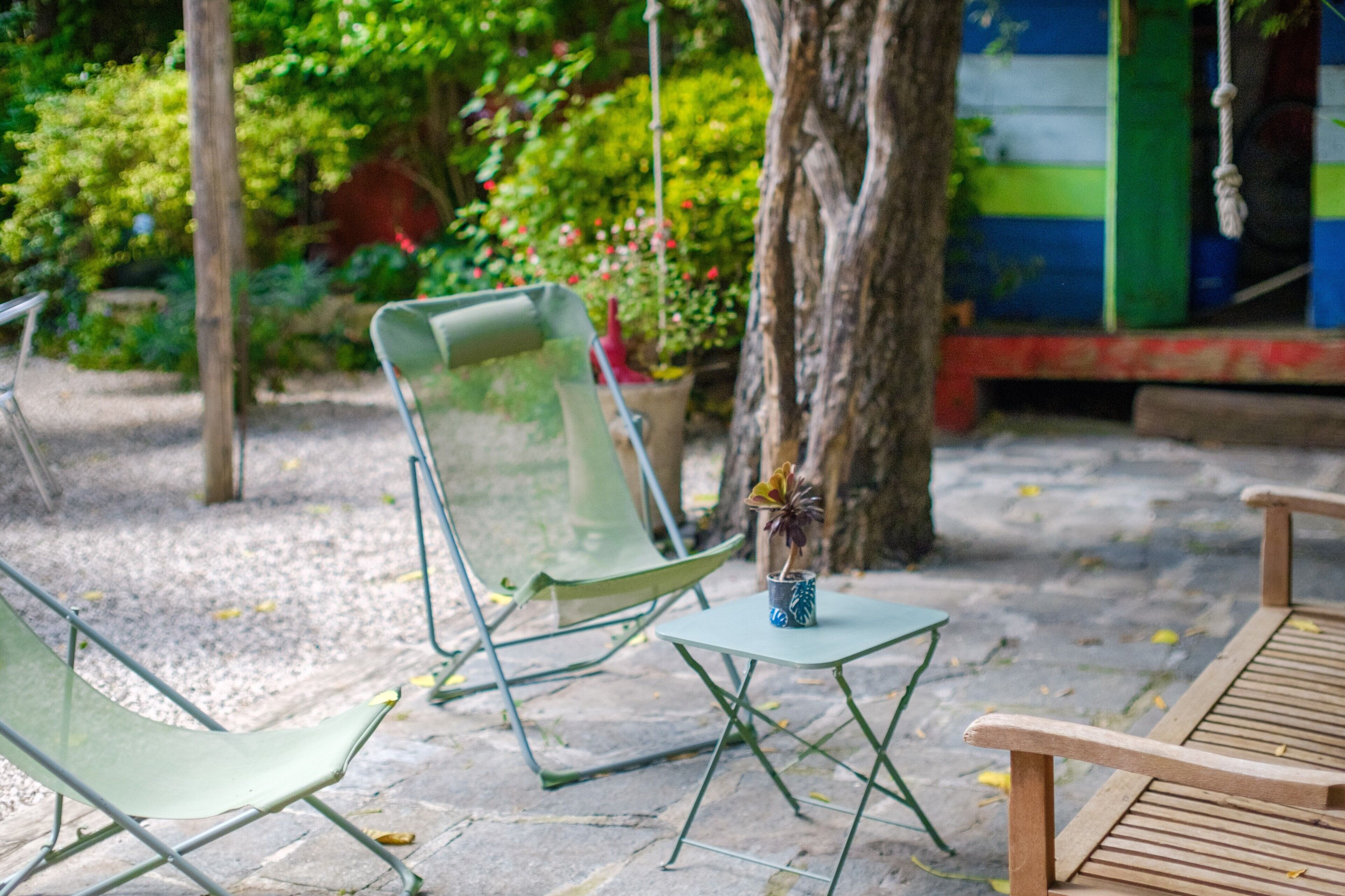 Une terrasse avec un banc en bois, une chaise en métal et une petite table sur laquelle est posée une plante en pot.
