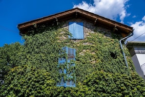 A stone building with wooden beams, a window with blue shutters, and ivy covering the walls.
