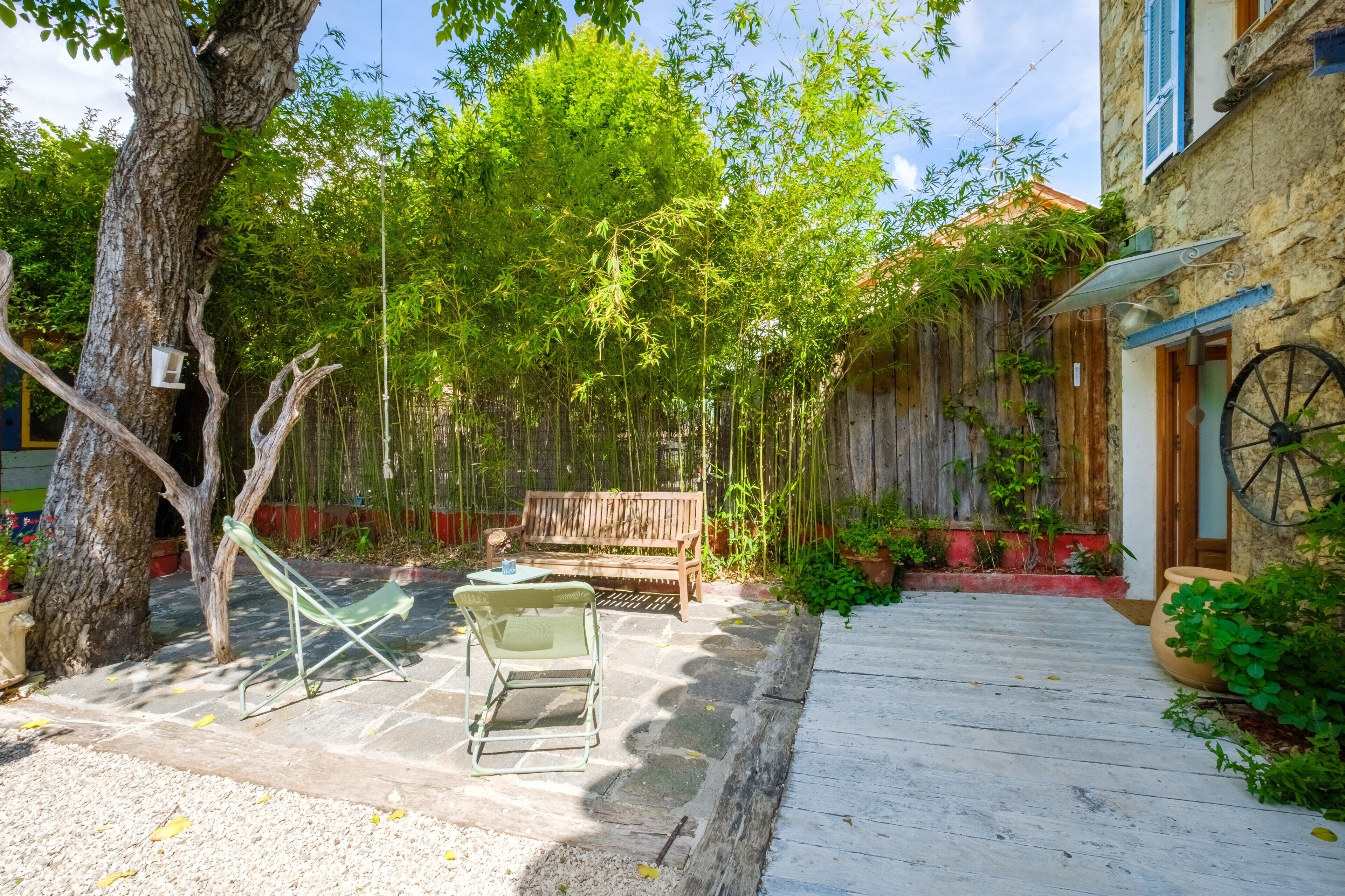A courtyard with a wooden bench, a green chair, and a small table.