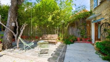 A courtyard with a wooden bench, a green chair, and a small table.