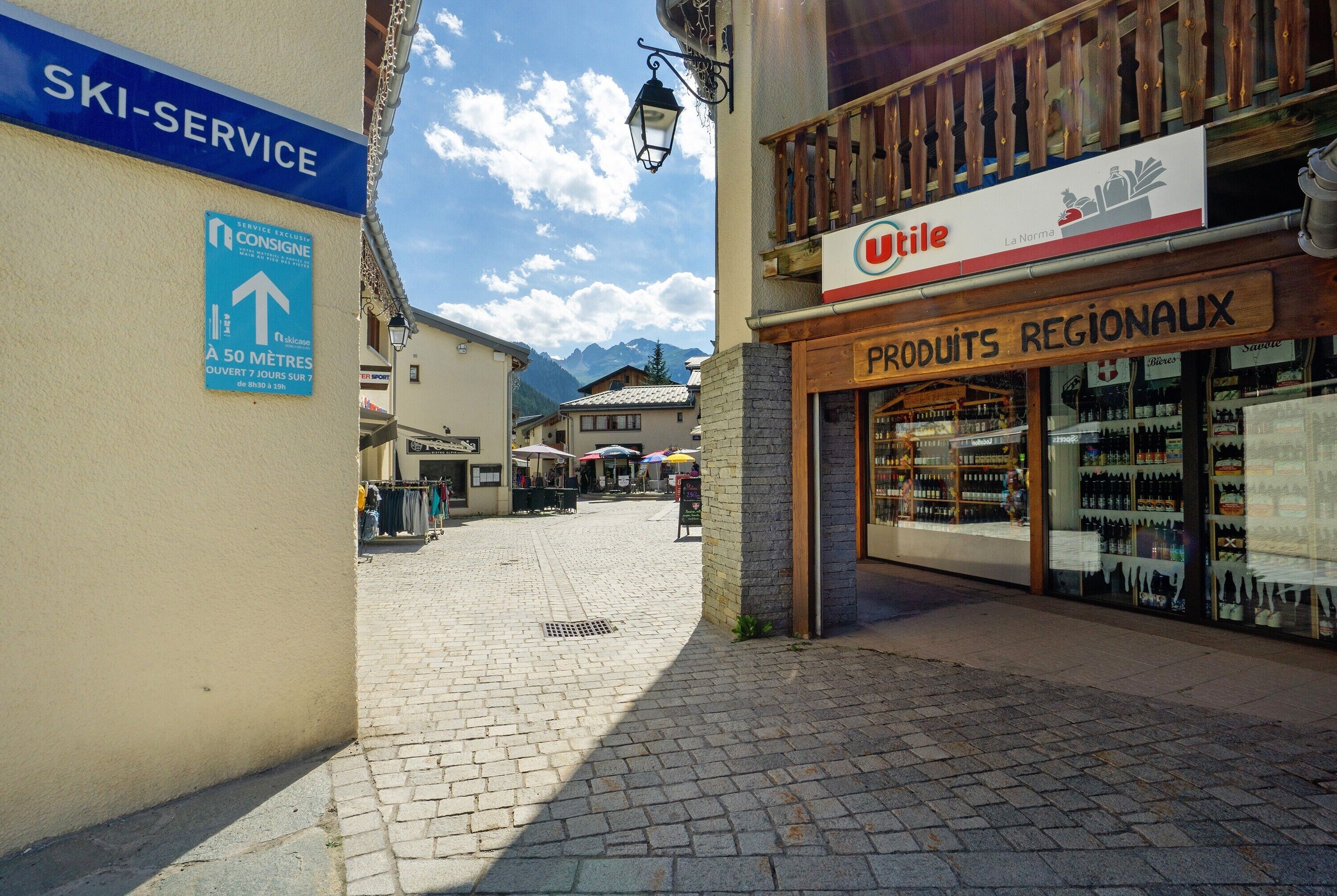 Una strada acciottolata con un cartello di deposito sci, un negozio di articoli di ferramenta e un negozio che vende prodotti tipici.