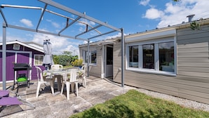 A covered patio area with a table and chairs, a purple building, and a beige house. - Mobile Home 'Mobilhome Rénové Sarzeau' with Private Terrace and Private Garden (Sarzeau)