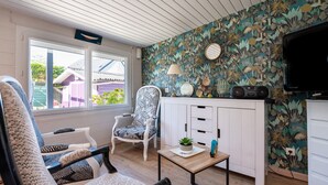 A room with a patterned wall, a white cabinet, a television, and a window with a view of a house. - Mobile Home 'Mobilhome Rénové Sarzeau' with Private Terrace and Private Garden (Sarzeau)