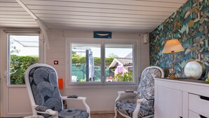 A room with two patterned chairs, a white cabinet, a table, and a window with a view of greenery and a building. - Mobile Home 'Mobilhome Rénové Sarzeau' with Private Terrace and Private Garden (Sarzeau)