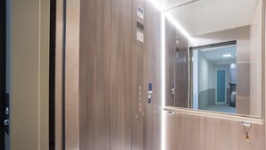 An elevator with a mirror, control panel, and emergency contact sign.