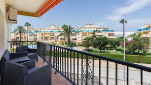 A balcony with wicker furniture, a pool, and a view of a hotel complex with multiple buildings and greenery.