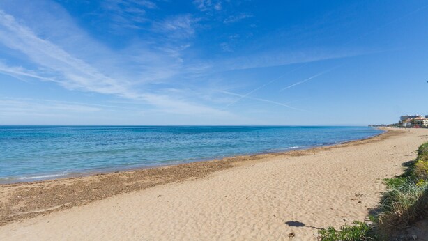 A beach with clear skies, a sandy shore, and buildings in the background.