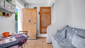 Une pièce comprenant un canapé, une table recouverte d’une nappe à motifs, une porte en bois et une étagère avec des bocaux.