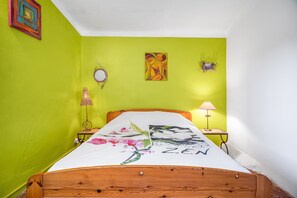 A room with a bed, a green wall, a small table with a lamp, and a painting.