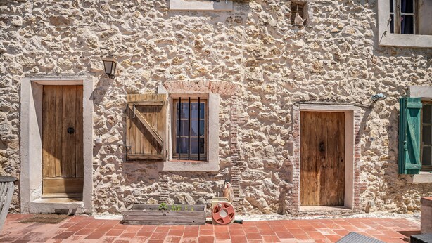 Un bâtiment en pierre doté de deux portes en bois et d’une fenêtre avec des volets.