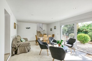 A modern living room with a dining area, a staircase, and a view of greenery.