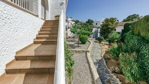 A white building with a staircase leading to a balcony, surrounded by greenery and a clear sky. - Holiday Home 'Amparo' with Sea Views, Private Pool and Wi-Fi (L'ESCALA)