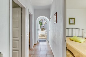 A hallway with a bed, a door, and an arched doorway leading to an outdoor area.