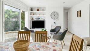 A modern living room with a TV, wooden chairs, a dining table, and a large window. - Holiday Home 'Amparo' with Sea Views, Private Pool and Wi-Fi (L'ESCALA)