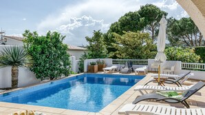 A swimming pool with lounge chairs and umbrellas, surrounded by greenery and a white fence. - Holiday Home 'Amparo' with Sea Views, Private Pool and Wi-Fi (L'ESCALA)