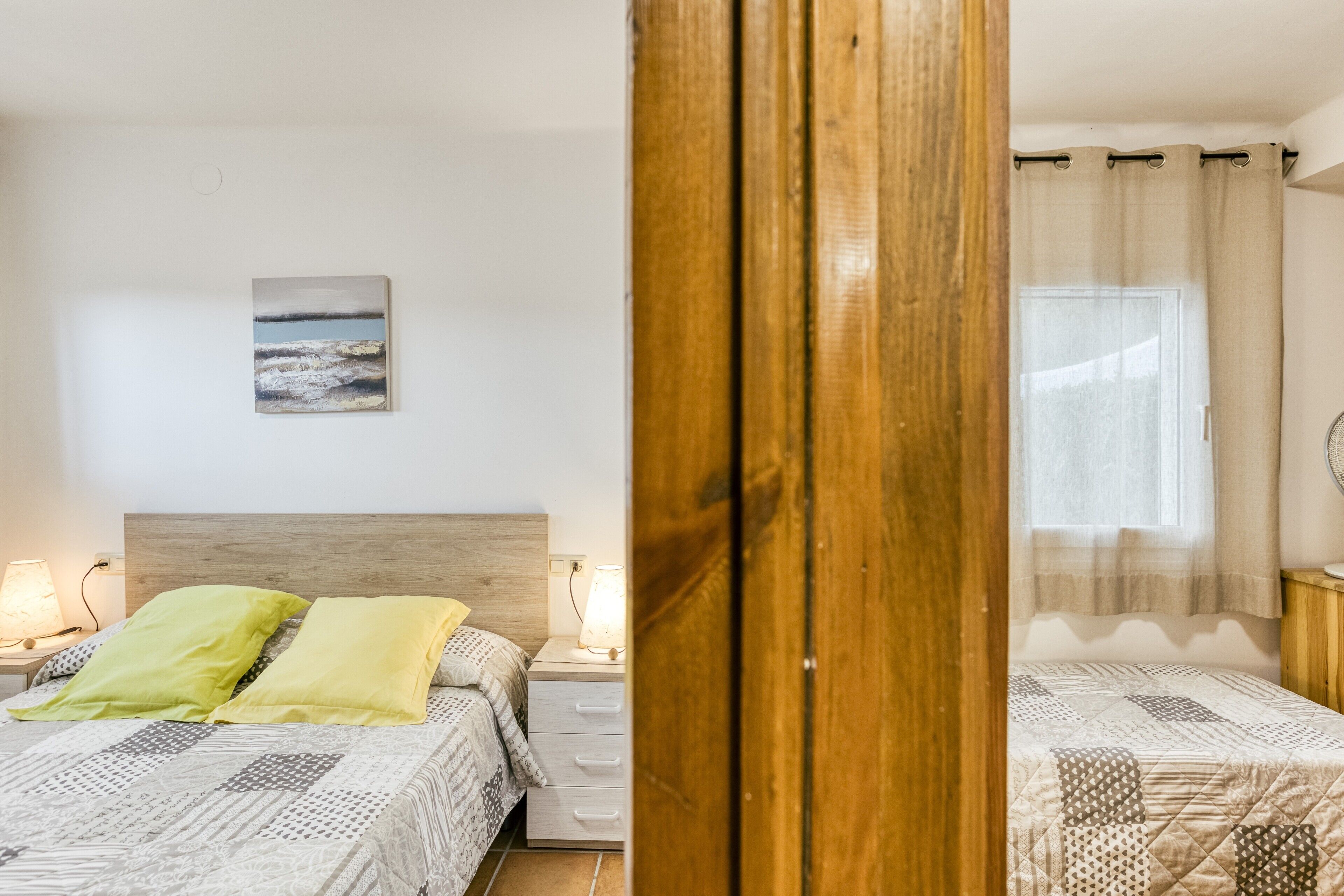 A bedroom with a bed, bedside tables, a lamp, a painting, and a window with curtains.