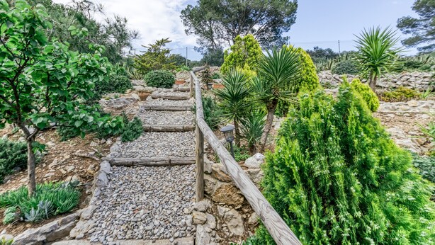 A garden pathway with a wooden fence, surrounded by various green plants and trees. - Holiday Home "Punta Montgó" with Sea Views, Private Pool and Wi-Fi (l'Escala)