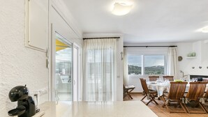 A kitchen with a coffee machine, a dining area with a table set for four, and a view of the outdoors through large windows. - Holiday Home "Punta Montgó" with Sea Views, Private Pool and Wi-Fi (l'Escala)