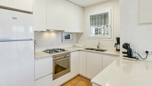 A modern kitchen with white cabinets, a gas stove, an oven, a microwave, a coffee maker, and a window with blinds. - Holiday Home "Punta Montgó" with Sea Views, Private Pool and Wi-Fi (l'Escala)