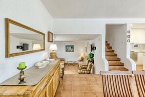 Ein großzügiger Wohnbereich mit Couch, Esstisch und Stühlen sowie einem Holztisch. Eine Treppe führt zu einer Küchenzeile.