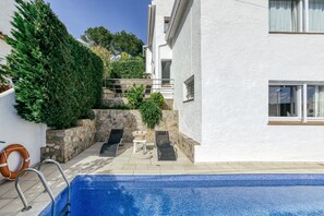 Ein Schwimmbecken mit Liegestühlen, einem Rettungsring und einer Steinmauer.