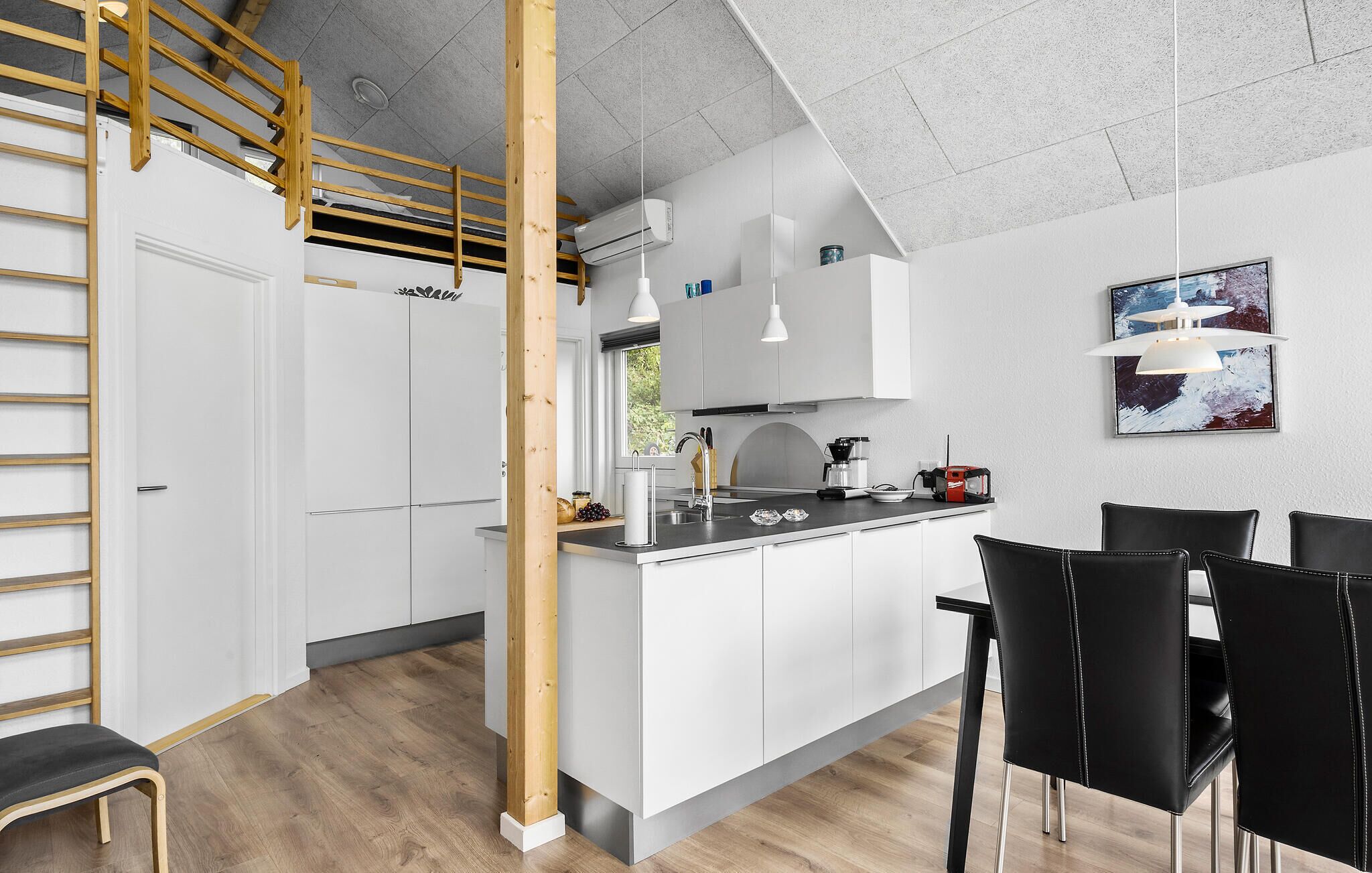 Une cuisine moderne avec des meubles blancs, un escalier en bois et un coin repas doté de chaises noires.
