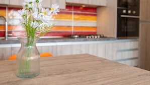 Una cocina con una mesa de madera, un florero de vidrio transparente y un salpicadero colorido.