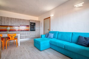 Une cuisine moderne dotée d’un four et d’un micro-ondes encastrés, un coin repas avec des chaises orange et un canapé turquoise.