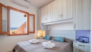 Un dormitorio con cama, mesita de noche, lámpara y vista al mar a través de una ventana.