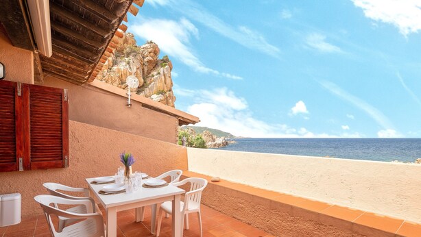 Una terraza con una mesa y sillas, con vista a una playa y acantilados rocosos.
