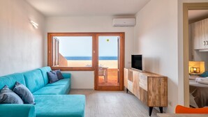 Una habitación con sofá, televisor, mueble de madera y vista a la playa.