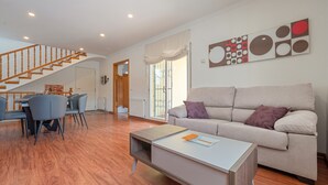 Amplia sala de estar con escalera de madera, un sofá, una mesa de centro y una mesa de comedor con sillas.