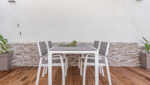 Una mesa blanca con cuatro sillas, una planta en maceta y un muro de piedra al fondo.