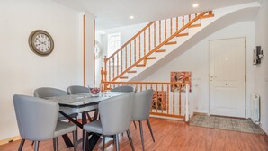 Un comedor con una mesa y sillas, una escalera con barandillas de madera y un reloj de pared.