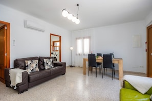 A living room with a brown leather sofa, a wooden dining table with chairs, a ceiling light fixture, and a white air conditioning unit. - Apartment 'Apartamento Imperial' with Wi-Fi and Air Conditioning (Colònia de Sant Jordi)