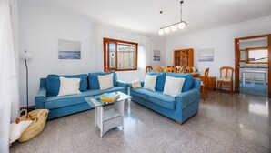 A living room with a blue sofa, a glass coffee table, and a wooden dining area. - Apartment 'Apartamento Cabrera' with Private Terrace, Wi-Fi and Air Conditioning (Colònia de Sant Jordi)